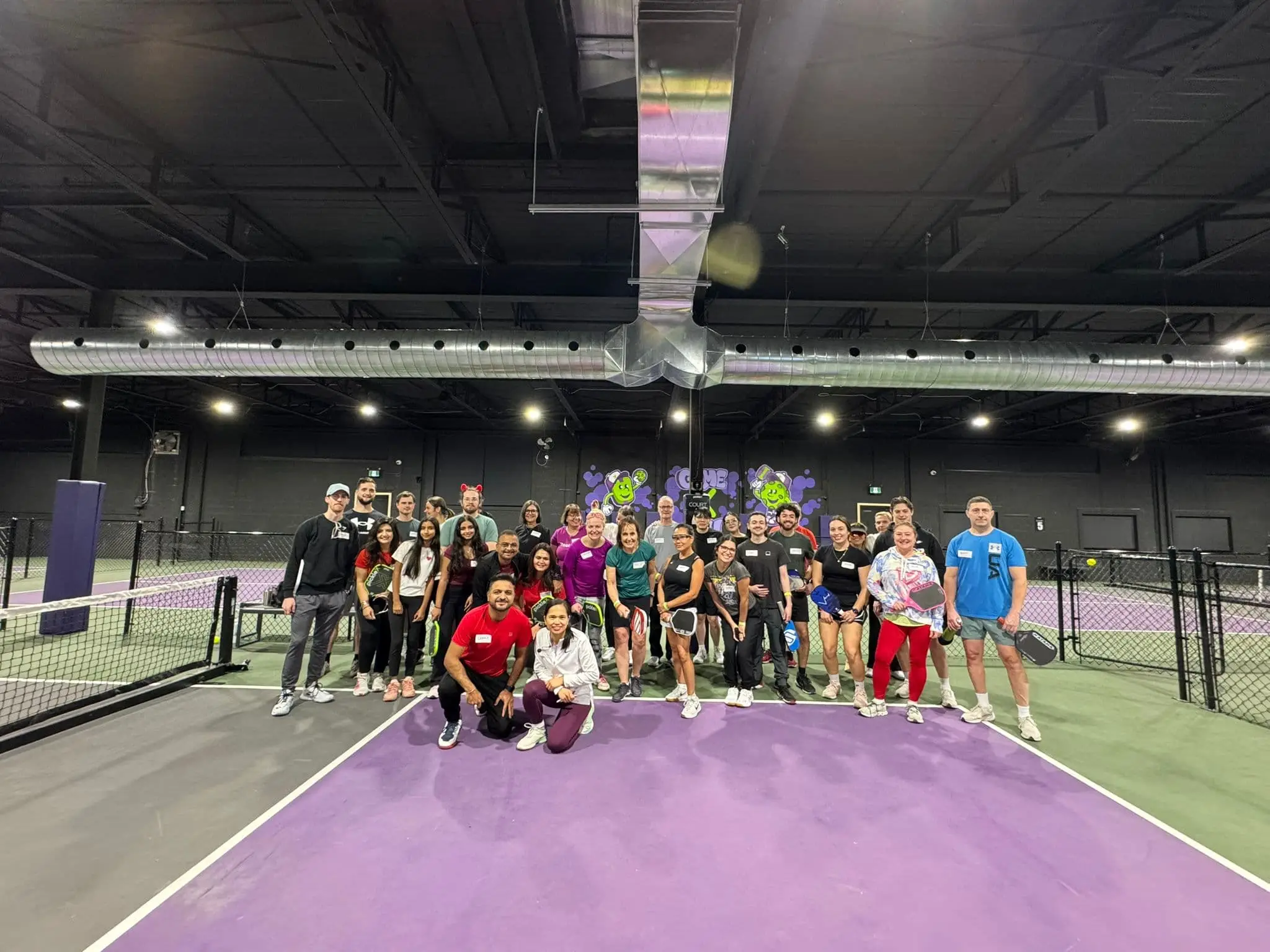 Group of pickleball players posing on a purple court inside the PickleXtreme indoor facility.